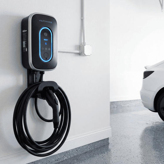 Level 2 EV charger mounted on white garage wall with Tesla in background