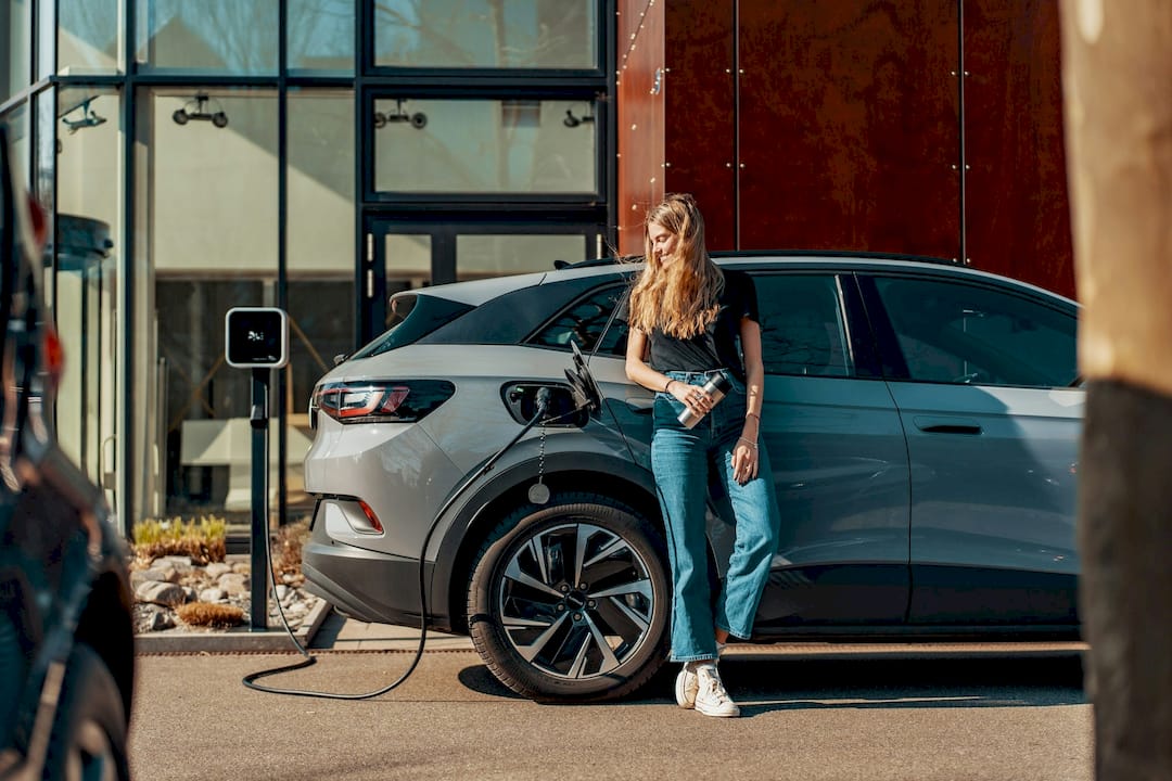Woman standing next to a charging electric vehicle in an urban setting